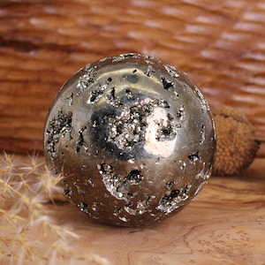Peut inclure: Une grande sphère de pyrite ronde et argentée avec une surface rugueuse et texturée. La sphère est composée de nombreux petits cristaux scintillants.