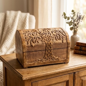 Könnte beinhalten: Braune Holzschatulle mit einem geschnitzten Baumdesign auf Deckel und Vorderseite. Die Truhe steht auf einem Holztisch. Der Hintergrund umfasst ein Fenster, eine Vase und Bücher. Die Truhe ist etwa 30 cm lang.