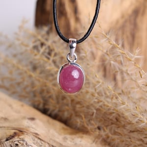 Könnte beinhalten: Eine silberne Halskette mit einem rosa ovalen Edelstein. Die Halskette ist an einem schwarzen Lederband.