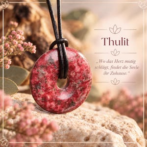 Könnte beinhalten: Ein kreisförmiger Thulit-Anhänger mit einer polierten, gesprenkelten rosa und grauen Oberfläche, der an einem schwarzen Band hängt. Der Text "Thulit" und "Wo das Herz mutig schlägt, findet die Seele ihr Zuhause." steht rechts im Bild.