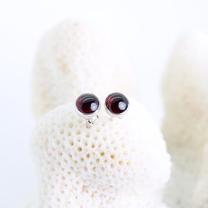 Op de afbeelding: Een paar zilveren oorbel studs met ronde, donkerrode edelstenen.