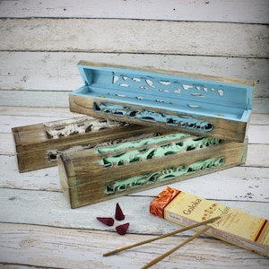 Può includere: Tre porta incensi in legno con intricati disegni intagliati. Il porta incensi superiore è azzurro, quello intermedio è bianco e quello inferiore è verde. I porta incensi sono impilati uno sopra l'altro. Nell'immagine ci sono bastoncini e coni di incenso.