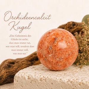 Könnte beinhalten: Eine polierte orangefarbene Calcitkugel mit weißen und dunklen mineralischen Einschlüssen. Der Text lautet: Orchideencalcit Kugel, Das Geheimnis des Glücks ist nicht, dass man immer tut, was man will, sondern dass man immer will, was man tut.
