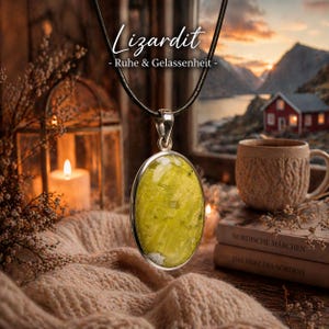 Pode incluir: Um colar com pingente com uma grande pedra ovalada verde-amarelada em uma moldura prateada. O pingente pende de um cordão preto. A palavra "Lizardit" está escrita em branco acima do pingente.