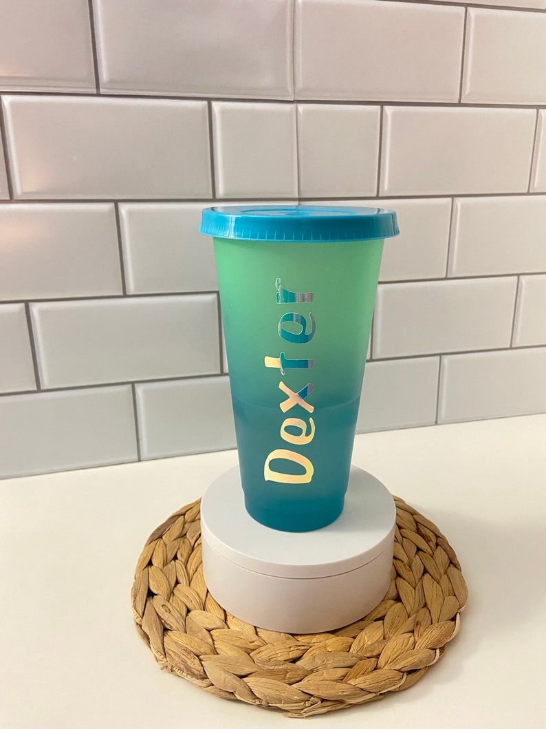 May include: A blue and green ombre reusable cup with a blue lid and the name "Dexter" written in gold foil lettering.