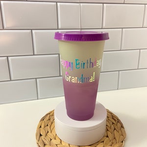 May include: A purple and white ombre reusable cup with a purple lid. The cup has the text "Happy Birthday Grandma!" in rainbow letters.