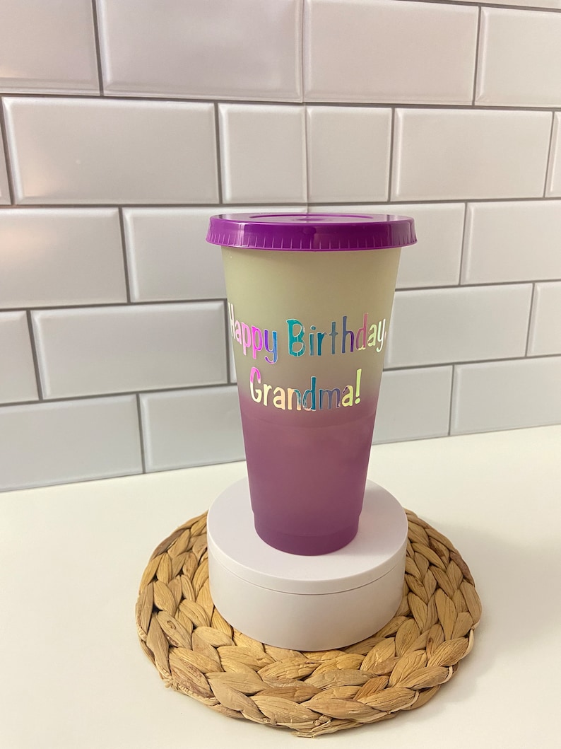 May include: A purple and white ombre reusable cup with a purple lid. The cup has the text "Happy Birthday Grandma!" in rainbow letters.