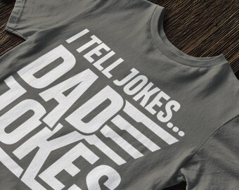 May include: A gray t-shirt with white text that reads "I tell jokes... DAD JOKES".