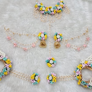 以下が含まれることがあります： ピンク、イエロー、ブルーの花を使った花のジュエリーセット。ネックレス、イヤリング、マングティカ、バングル2つが含まれています。