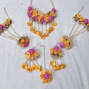 以下が含まれることがあります： 黄色とピンクの花のジュエリーセット。ネックレス、ブレスレット2本、イヤリング1ペア。人工の花と金色のビーズで作られています。