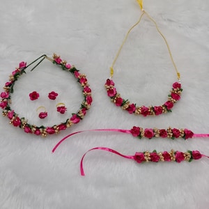 以下が含まれることがあります： ヘッドバンド、ネックレス、ブレスレット2本のピンクの花のジュエリーセット。ジュエリーは小さなピンクの花とゴールドのアクセントでできています。
