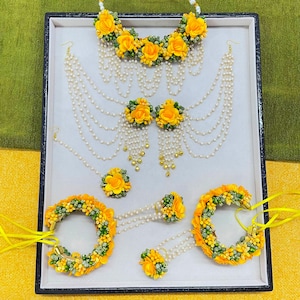 May include: A complete floral jewelry set featuring a necklace, earrings, bracelets, and rings. The set is adorned with yellow flowers, white pearls, and green accents. The jewelry is arranged on a white surface.