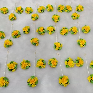 以下が含まれることがあります： 真珠のチェーンが付いた黄色と緑の花のイヤリング24個セット。イヤリングは白い表面に並べてあります。