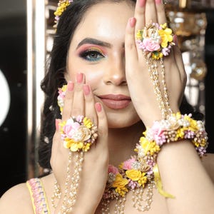 以下が含まれることがあります： 黄色、ピンク、白の花を使った花のジュエリーセット。ネックレス、ブレスレット、2つの指輪が含まれています。