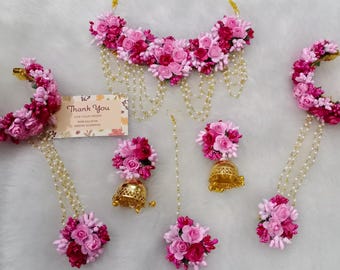 Könnte beinhalten: Ein rosafarbenes und weißes Blumen-Schmuckset mit einer Halskette, Ohrringen und zwei Haarteilen. Der Schmuck ist aus künstlichen Blumen und Perlen gefertigt.