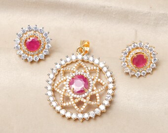 Può includere: Un set di collana con ciondolo in oro con una pietra di rubino rossa rotonda circondata da pietre di zircone cubico bianche. Il ciondolo presenta un design floreale e gli orecchini sono semplici perni con un solo rubino rosso.