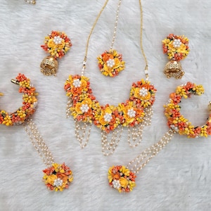 May include: A floral jewellery set featuring a necklace, earrings, bangles, and a maang tikka. The flowers are crafted from fabric and are in shades of yellow and orange.