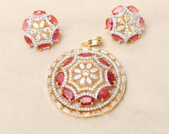 Può includere: Un set di collana con ciondolo in oro con pietre di zircone cubico rosse e bianche. Il ciondolo è di forma rotonda con un fiore al centro. Gli orecchini sono piccoli e rotondi con un motivo a fiore.