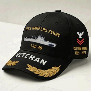 以下が含まれることがあります： USS HARPERS FERRYとLSD-49の刺繍と船のイラストが施された黒い野球帽。つばには金色の月桂樹の葉と共にVETERANの文字が刺繍されている。側面には白い鷲と赤いシェブロンのマークとテキストがデザインされている。