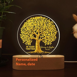 May include: A personalized wooden night light with a circular design featuring a golden tree illustration. The text reads "50 YEARS TOGETHER" and includes names and a date. The base of the light has the text "Personalized Name, date".