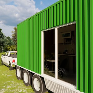 May include: A green shipping container home with a large window revealing a kitchen interior. The home is being towed by a white pickup truck on a grassy lawn.
