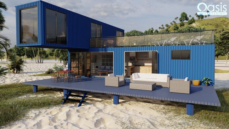 A blue container home with a wooden deck and patio furniture. The home has a large window and a glass door leading to the interior. The deck is made of wood and has a railing. The patio furniture includes a white couch, two armchairs, and a coffee table. The home is situated on a sandy beach with green grass and palm trees in the background. The text 'Oasis Container Living' is visible on the side of the home.
