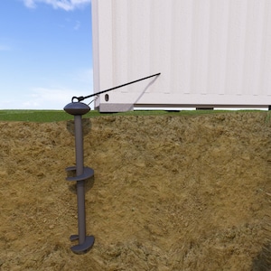 May include: A ground anchor with a metal screw and a black strap attached to a white container. The anchor is partially buried in the ground.