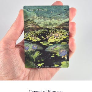 Puede incluir: Una tarjeta coleccionable rectangular titulada Carpet of Flowers que muestra un estanque oscuro lleno de nenúfares verdes, flores violetas y una pequeña rana verde. La escena incluye libélulas, un cielo nocturno y el texto Céline Combes Alters.