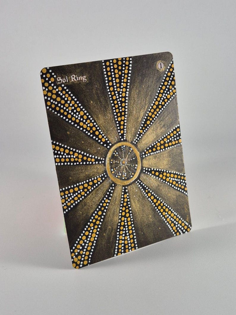 May include: A rectangular game card titled Sol Ring with the number 1 in the top right corner. The card features a dark brown background with a central gold circle and radiating lines composed of small white and yellow dots in a sunburst pattern.