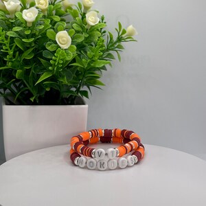 May include: Two bracelets with orange and maroon beads, spelling out "VT" and "HOKIES" in white letters.