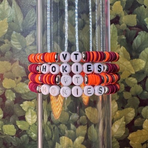 May include: Three stacked bracelets with orange, maroon, and white beads. The beads spell out "VT" and "HOKIES".