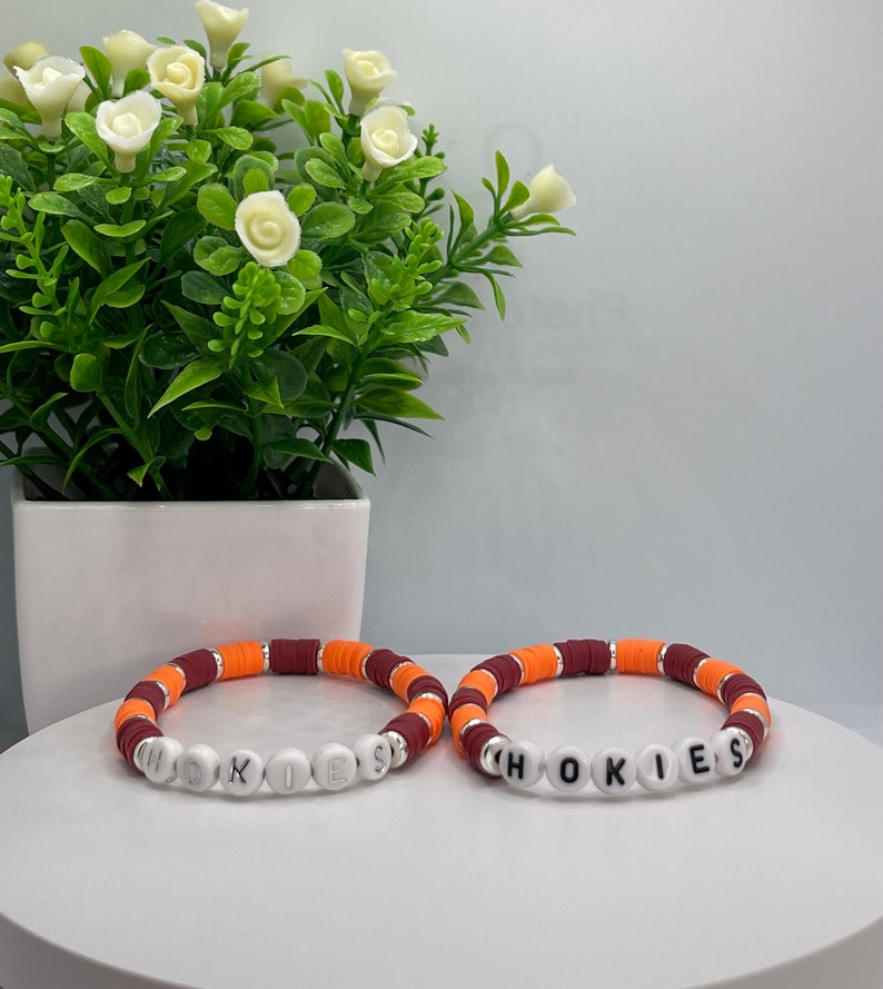May include: Two beaded bracelets with the word "HOKIES" spelled out in white beads. The bracelets are made with maroon, orange, and white beads.