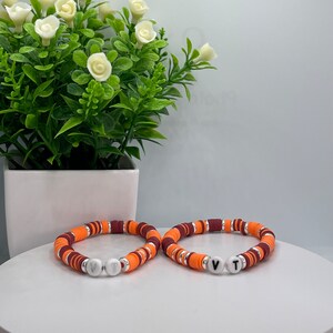 May include: Two orange, maroon, and silver beaded bracelets with white letter beads spelling "VT".