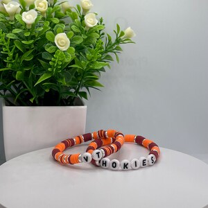 May include: Two bracelets made of orange and maroon beads with the word "HOKIES" spelled out in white letters.