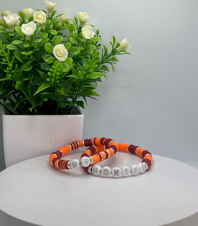 May include: Two bracelets with orange, maroon, and white beads. The bracelets spell out "VT" and "HOKIES".