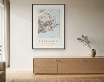 May include: A framed wall art print featuring a topographic map of Rio de Janeiro. The map displays land in shades of beige and grey with a light blue ocean area. Below the map, the text reads RIO DE JANEIRO with coordinates and elevation.