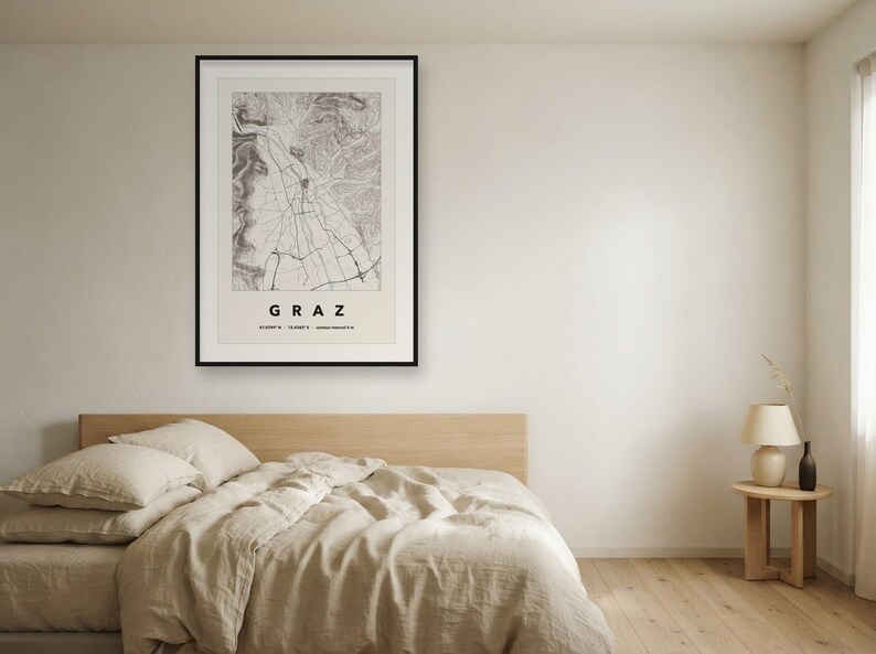 May include: A framed wall art print featuring a detailed black and white topographic map of Graz, Austria. The print includes the city name GRAZ in bold capital letters at the bottom, along with geographic coordinates and elevation data.