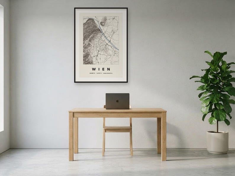 May include: A framed wall art print featuring a detailed black and white map of Vienna, Austria, with the text WIEN and geographic coordinates printed below the map. The print is displayed in a thin black frame on a plain light-coloured wall.