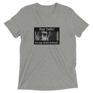 Könnte beinhalten: Ein heidefarbenes T-Shirt mit einem Schwarzweißbild eines Männergesichts und dem Text "Say 'hello' to my little friend!"
