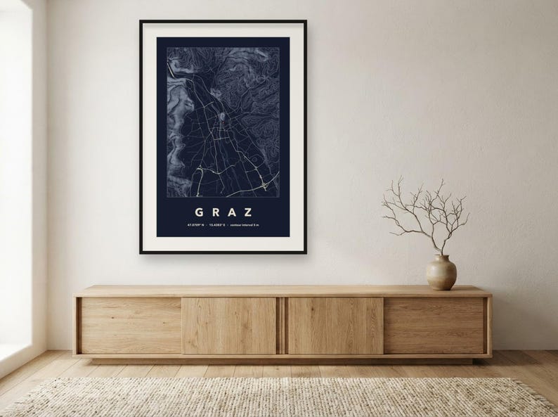 May include: A framed wall art print featuring a dark blue map of Graz, Austria. The map displays white street lines and topographic contours. Below the map, the text reads GRAZ, followed by the coordinates 47.0707 N, 15.4395 E.
