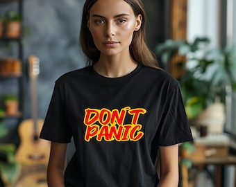 May include: Black t-shirt with the words "DON'T PANIC" in red and yellow lettering. The shirt is a crew neck style and appears to be made of a soft material. The text is in a bold, stylized font.