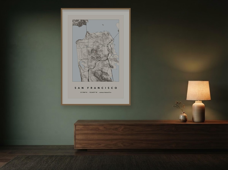May include: A framed wall art print featuring a topographic map of San Francisco. The map displays detailed terrain lines in black against a light blue background, with the text SAN FRANCISCO and coordinates printed in black at the bottom.