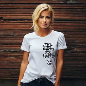 Peut inclure: Une femme portant un t-shirt blanc avec le texte "Do what makes you happy!" et un smiley. Elle est debout devant un mur en bois.