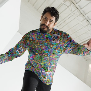 Könnte beinhalten: Ein Langarmshirt mit einem bunten, allover-Druck von Comic-Gesichtern. Das Shirt ist ein lebendiger Mix aus Blau, Grün, Lila und Gelb.