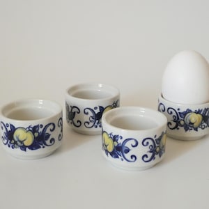 Peut inclure: Ensemble de quatre coquetiers en céramique blanche avec des motifs floraux bleus et jaunes. Un coquetier contient un œuf blanc.