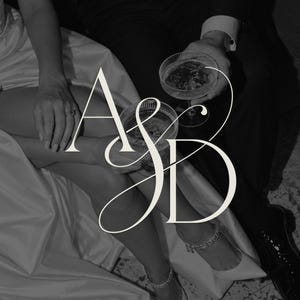 Puede incluir: Una fotografía en blanco y negro que muestra a dos personas con vestimenta formal, una con un vestido de satén y la otra con traje, sosteniendo copas de cristal estriado. El gran monograma blanco con serifas A&D se superpone al centro.