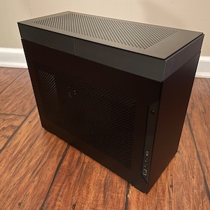 May include: A black computer case with a mesh front panel and a top panel with a mesh design. The case has a USB port and a headphone jack on the front.