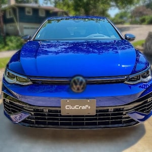 Peut inclure: Une voiture à hayon Volkswagen bleu vif vue de face. Le véhicule présente une finition brillante, des phares angulaires nets, une calandre noire et un support de plaque d'immatriculation avec le texte CluCraft centré sur le pare-chocs avant.