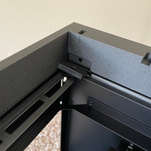 May include: Close-up of a black computer case with a metal rail system and a black metal bracket. The case has a textured finish.