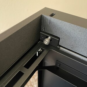 May include: Close-up of a black computer case with a metal screw securing a panel. The screw is silver and has a hexagonal head.